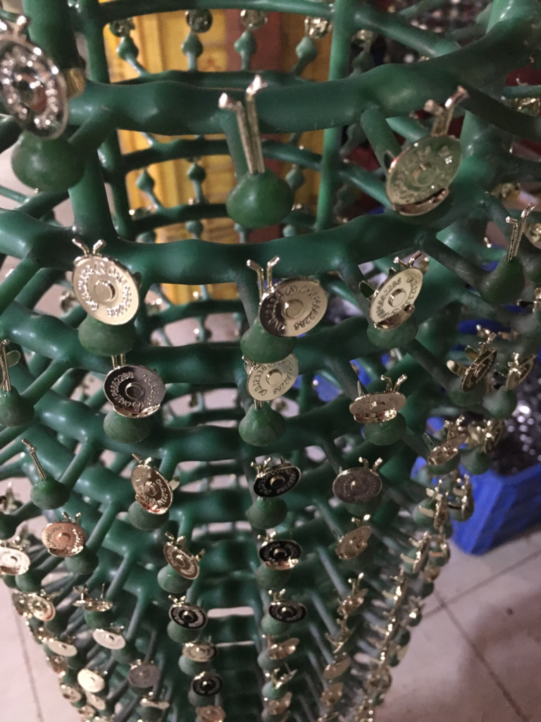 Freshly electroplated male magnetic snap buttons hanging on a plating rack, showcasing a high-quality finishing process before removal.