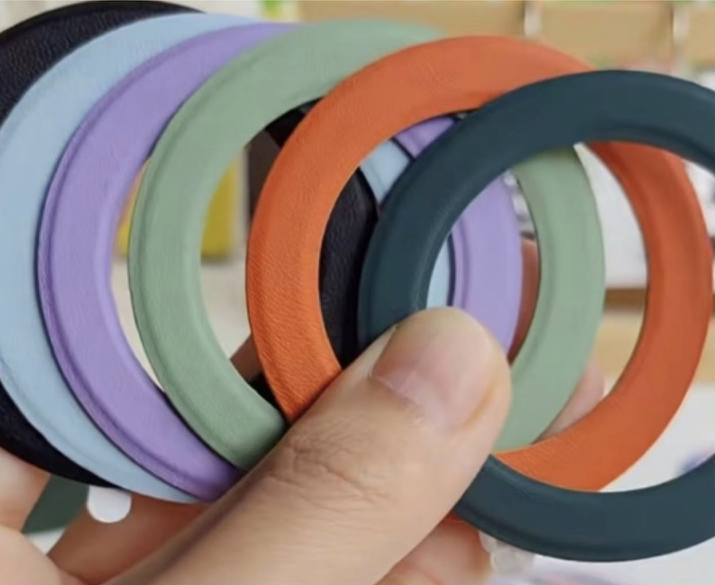 A hand holding colorful magnetic metal ring plates clad in PU leather, showcasing textures and finishes for premium magnetic applications.