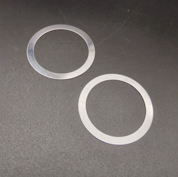 Two silver metal washers lie on a dark surface, one lighter and one darker in color.